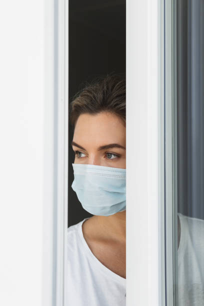 istock Scared woman wearing prevention mask looking outside through the 1290266819