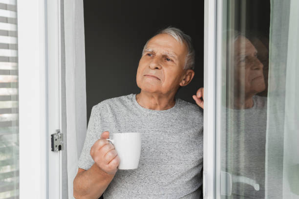 istock Elderly man with a cup of coffee looking into the window 1290267069