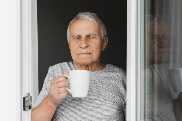 istock Elderly man with a cup of coffee looking into the window 1290267586