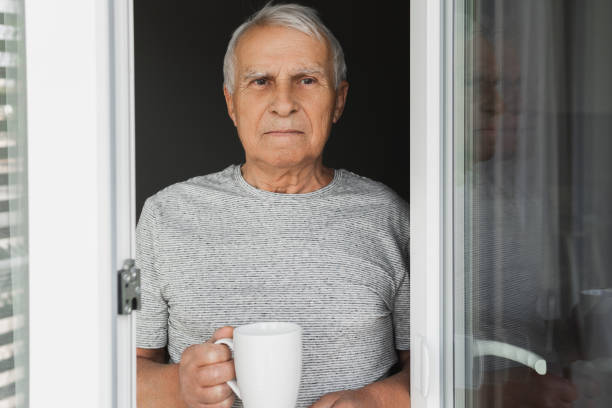 istock Elderly man with a cup of coffee looking into the window 1290267597