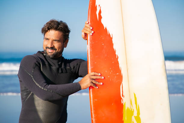 istock Happy man in swimsuit standing with surfboard and looking away 1290267680