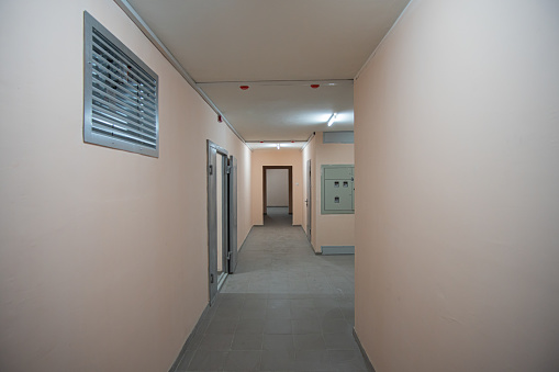 Hallway of apartment building with ventilation on foreground and many doors and no people. Interior of multifamily apartment building.