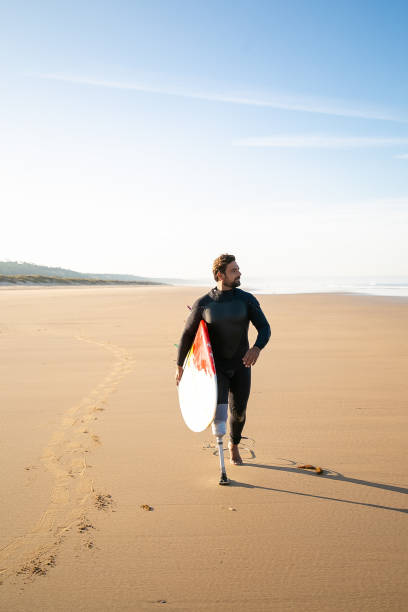 istock Active surfer with amputated leg walking on beach with surfboard 1290269486