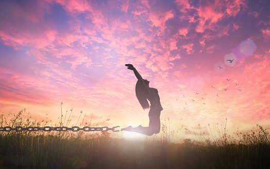 Silhouette of a woman jumping and broken chains at orange meadow autumn sunset background