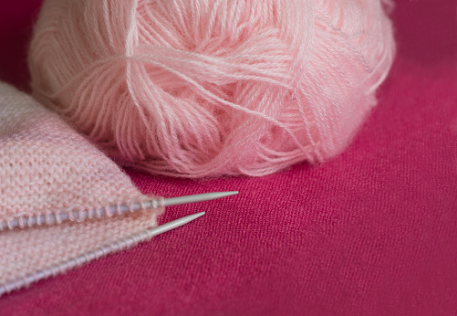 Pink ball of yarn and two knitting needles on a burgundy background
