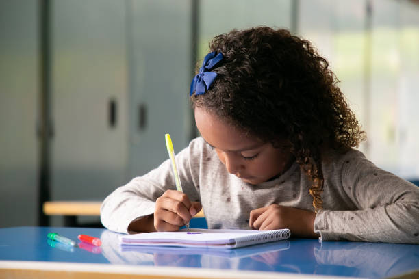 istock Focused curly haired schoolgirl sitting at desk 1290277749