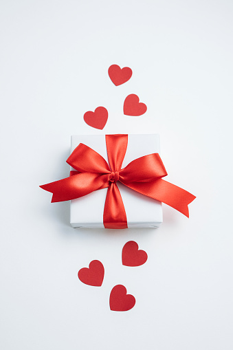 Gift box with red ribbon and hearts on white background. Valentines day background. Top view, flat lay. Vertical.