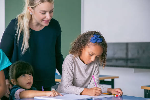 istock Cheerful female school teacher watching girls doing their task 1290279037
