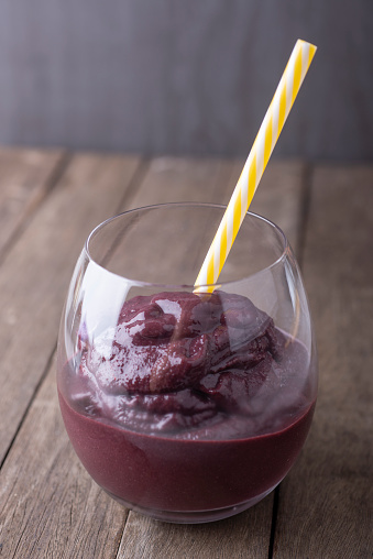 Brazilian typical acai juice into a glass with straw over wooden background.