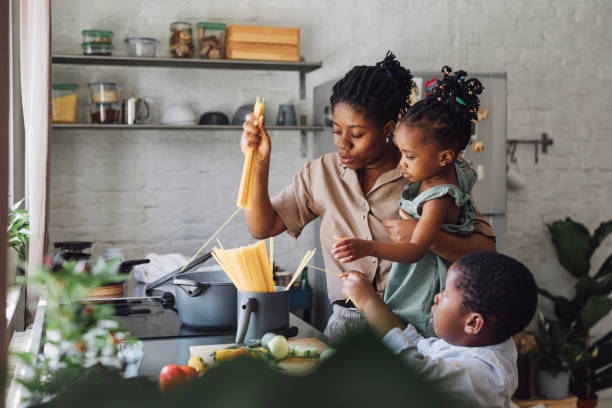 istock Mother, Daughter and Son Preparing Spaghetti and Vegetables for Lunch over a Cutting Board 1290287563