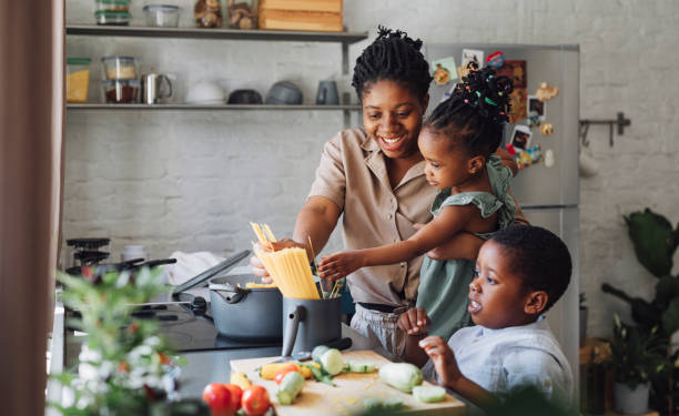 moeder, dochter en zoon die spaghetti en groenten voor lunch bereiden over een snijdende raad - keuken fotos stockfoto's en -beelden