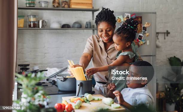 Mother Daughter And Son Preparing Spaghetti And Vegetables For Lunch Over A Cutting Board Stock Photo - Download Image Now
