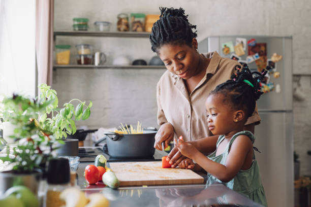 istock Mother and Daughter Cutting a Tomato for Lunch in a Kitchen 1290287573
