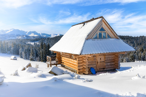 An old snow-covered log house on a hill with a winter sunset on the wall.