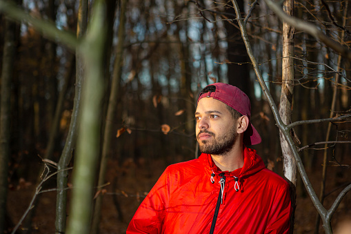 Young man poses for profile portrait outdoors in the forest. His head is facing the sunlight.