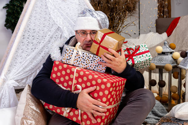 istock middle-aged man with glasses and a silver dwarf hat with Christmas gift boxes in a decorated room 1290301224