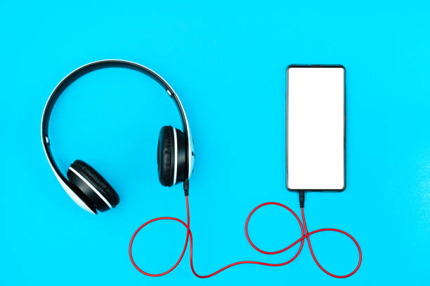 istock Flat lay smartphone, mobile with headphones on a blue background, copy space. White screen display on device for design music application presentation. 1290302372