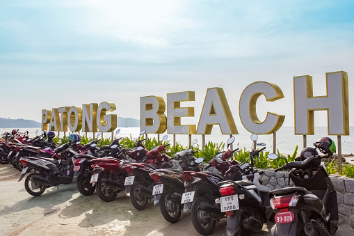 Thailand, Phuket - January 10, 2020 - motorbikes near the Patong Beach signage against the background of a clear sky