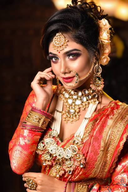 Portrait of very beautiful young Indian bride in luxurious bridal costume with makeup and heavy jewellery in studio lighting indoor Portrait of very beautiful young Indian bride in luxurious bridal costume with makeup and heavy jewellery in studio lighting indoor traditional clothing photos stock pictures, royalty-free photos & images