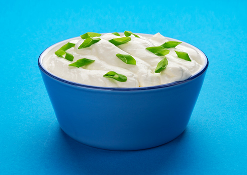 Bowl of sour cream with onion on blue background