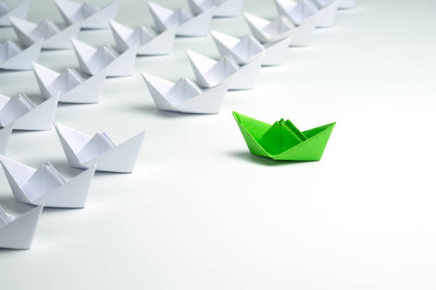 Leadership concept with Green paper ship standing out from the group of white ships on white background. stock photo