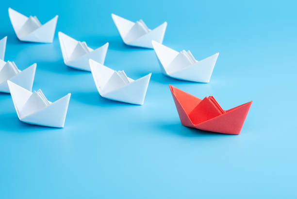 istock Leadership concept. Red leader paper ship leading among white on blue background. 1290307962