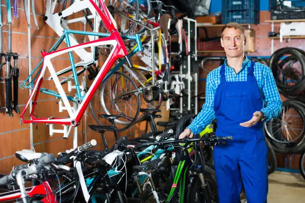 cheerful smiling man seller wearing uniform fixing bike in bike store