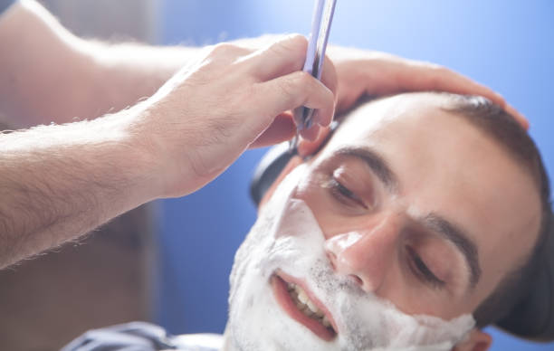 istock Hand of barber holding razor and shaving a client. 1290313656