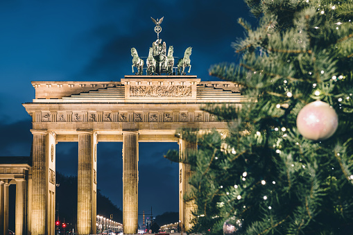 golden illuminated Brandenburger Tor behind tall festive shining christmas tree at blue hour