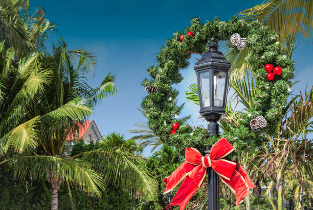 Christmas wreath decoration on a street lamp post in Key West, Florida. Fake wreath with fir green, red baubles and pine cones, finished with a red bow. Christmas wreath around lantern lamp at a tropical vacation destination with palm trees in Key West, Florida, USA florida christmas stock pictures, royalty-free photos & images