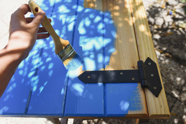 istock Hand with paint brush painting a pine wood shutter in blue 1290316984