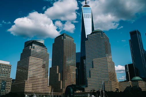 Architectural view of modern glass skyscrapers and One World Trade Center building against cloudy blue sky in Manhattan New York