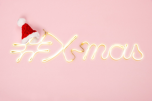 Santa hat with neon letters # Christmas on pink background