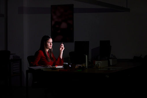 Serious businesswoman sitting at desk. Female executive working late. She is in dark office.