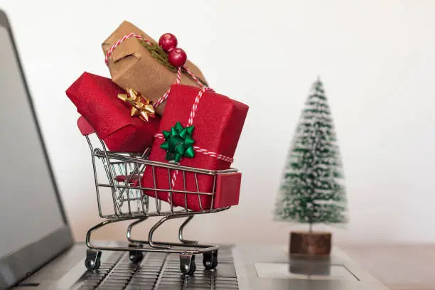 Photo of Shopping cart with christmas gifts on laptop computer with christmas tree on the background. Online shopping, e-commerce and worldwide shipping concept