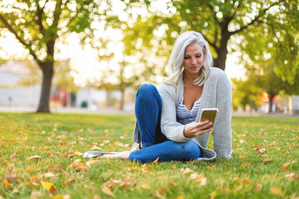 In Western Colorado Attractive Millennial Female with Platinum Blonde Hair Outdoors on a Sunny Late Summer Early Fall Day in Park Setting Using Smart Phone Technology Part of a Series (Shot with Canon 5DS 50.6mp photos professionally retouched - Lightroom / Photoshop - original size 5792 x 8688 downsampled as needed for clarity and select focus used for dramatic effect)