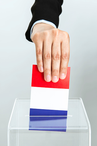 Hand of business person  is inserting French flag into ballot box. Representing votes of business people in France.