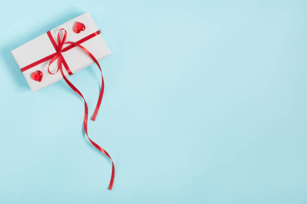 istock Gift box wrapped in a white paper with red ribbon bow on blue background top view. 1290329302