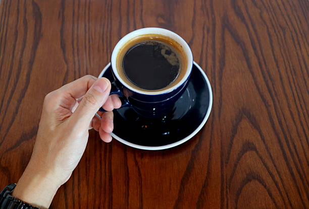 Man's Hand Holding the Cup of Hot Coffee Served on Wooden Table