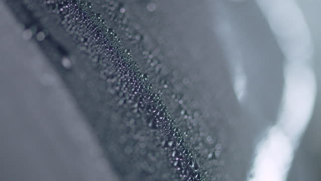 Shiny, dark metal sheet covered with water drops. Pouring rain. Extreme close up