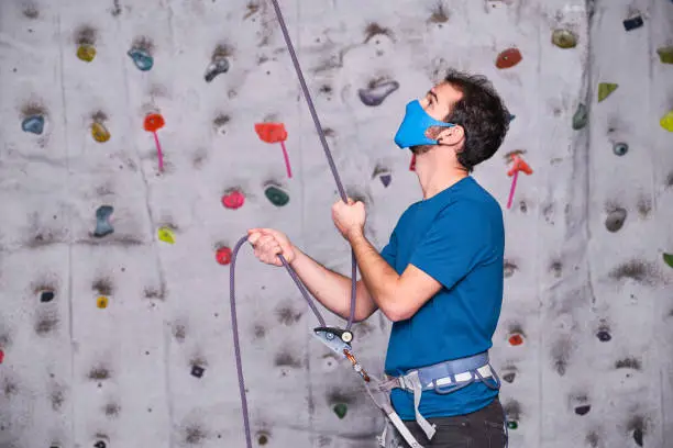 Photo of Male climber wearing protective face mask securing another climber