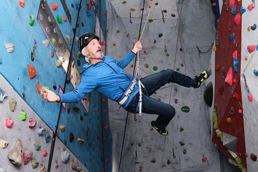 Professional senior man flying after jump while he is climbing on an artificial rock climbing wall. Extreme sports concept.