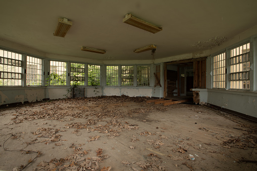 Abandoned school building interior with damaged floors and ceilings. Light is coming in through the dirty and damaged windows.