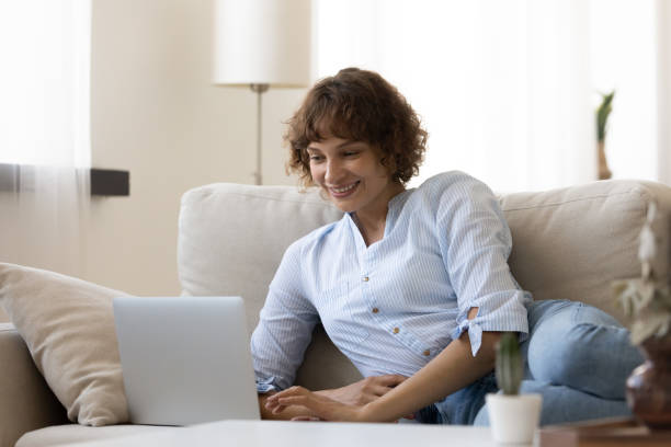 istock Smiling young woman looking at laptop screen, lying on couch 1290335540