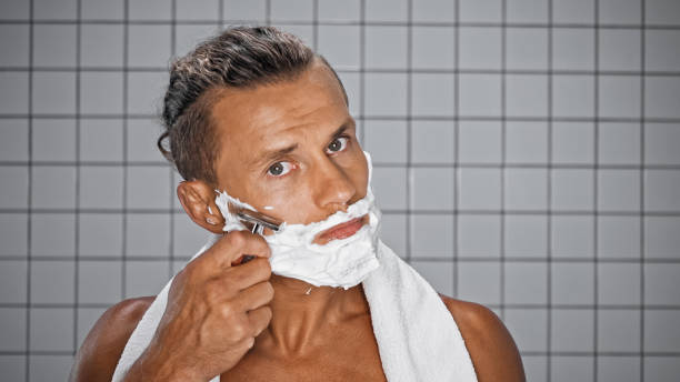 istock shirtless man shaving and looking at camera in bathroom 1290341349