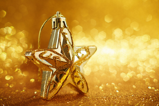 Star shaped christmas ornament on shiny gold colored background with lots of bokeh balls.Holiday concept backdrop with twinkling bright bokeh circles. Selective focus, shallow depth of field