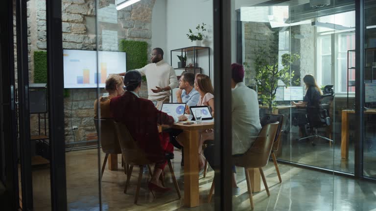 Office Conference Room Meeting: Male Chief Executive Talking to a Diverse Team of Professional Businesspeople. Creative People Listen to CEO Discuss Design, Data Analysis, Plan Marketing Strategy