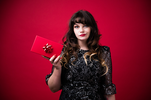 Stylish girl in fancy silver black dress who receives a red gift box for Christmas, but she doesn't like it. A disappointing present in a red box.