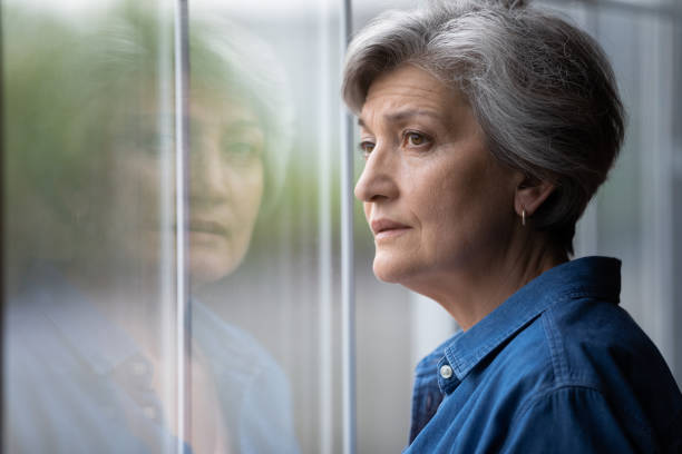 da vicino pensieroso sconvolto donna matura guardando fuori dalla finestra - senior women depression sadness women foto e immagini stock