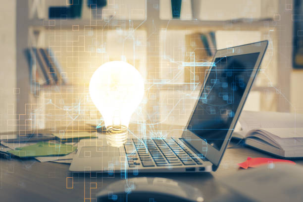 istock Computer on desktop in office with bulb icon hologram. Multi exposure. Concept of idea. 1290348670
